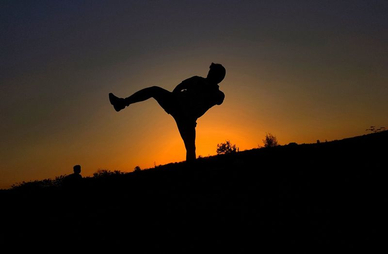 Silhouette of man kickboxing at field against sky during sunset