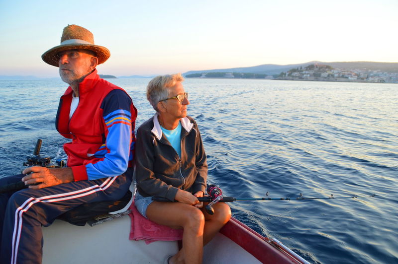 Senior man and woman sitting on boat in river against sky