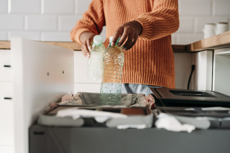 Hands of girl putting plastic bottles in recycling bin at home