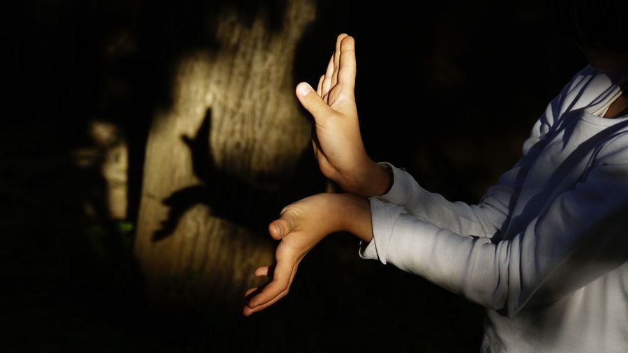 Midsection of person gesturing by wall at night