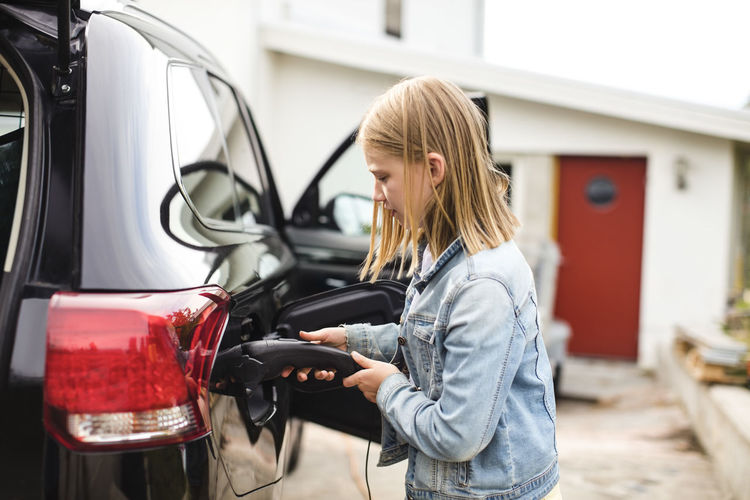 Side view of blond girl charging electric car in driveway