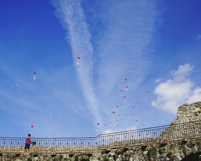 Men standing by stone wall and looking at heart shaped balloons with message