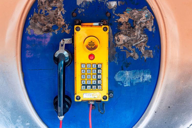 Old, rusted blue telephone booth with old yellow phone inside.