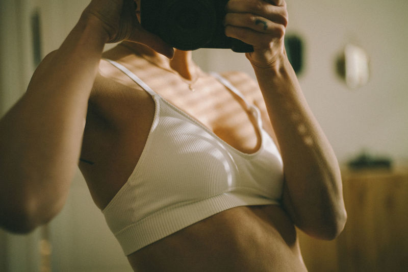 Midsection of woman in the bra in the mirror, standing at home