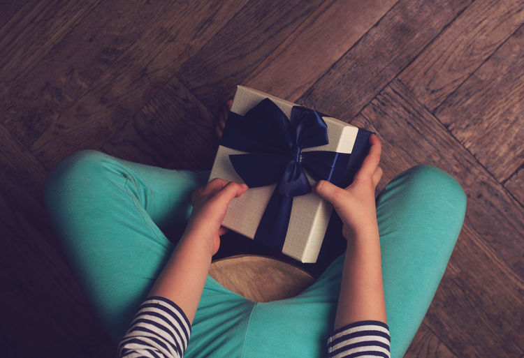 Low section of girl holding gift box while sitting on hardwood floor