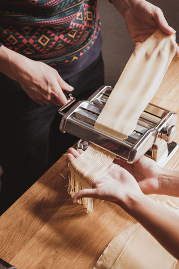 Cropped image of women preparing pasta with machine in kitchen