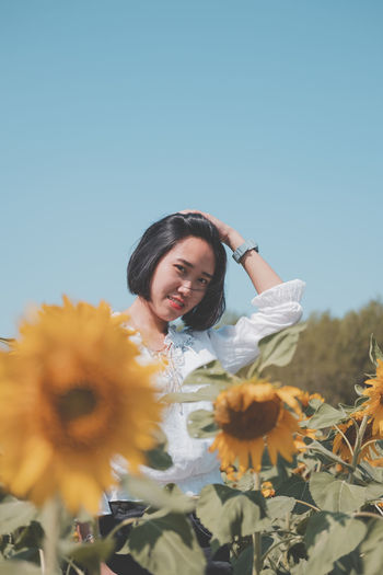 Portrait of smiling woman with sunflower against sky