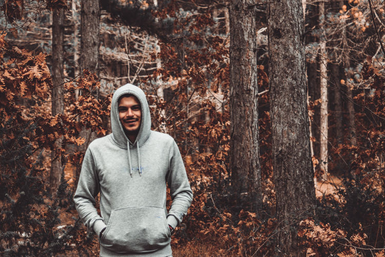 Portrait of smiling man standing by tree trunk in forest