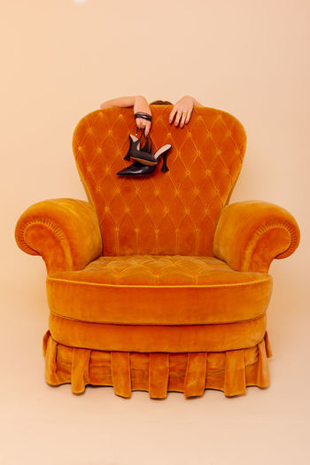 Tired woman holding shoes behind the sofa. while standing behind the yellow sofa. photo in studio. 
