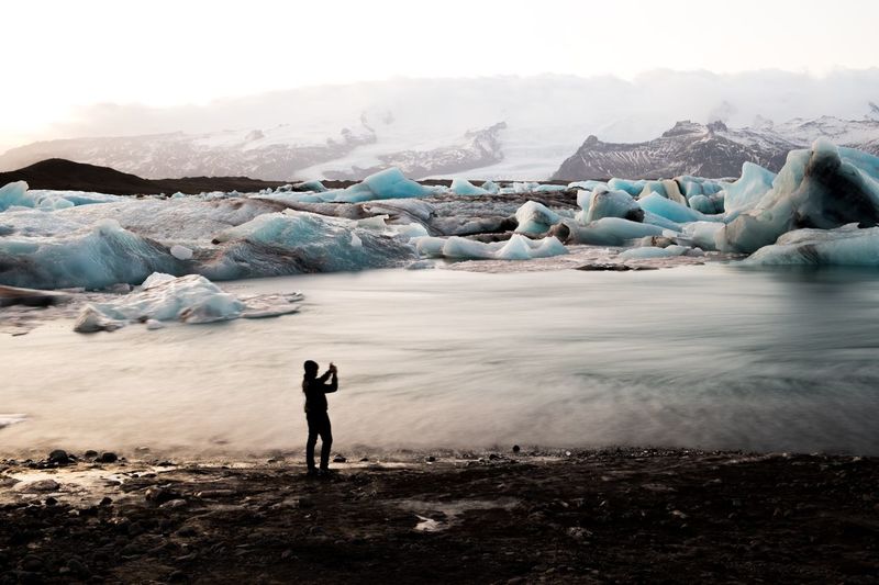 Silhouette woman photographing snowcapped mountain at jokulsarlon glacial lagoon