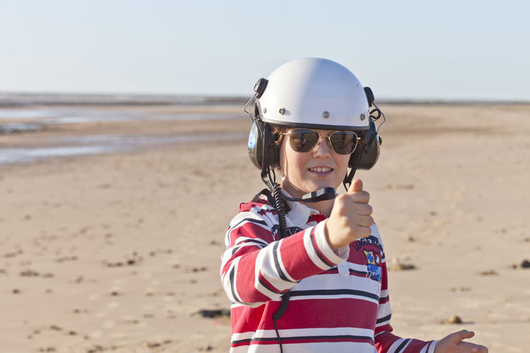 Portrait of smiling boy wearing sunglasses and helmet at beach against sky