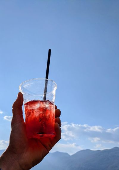 Midsection of person holding drink against blue sky