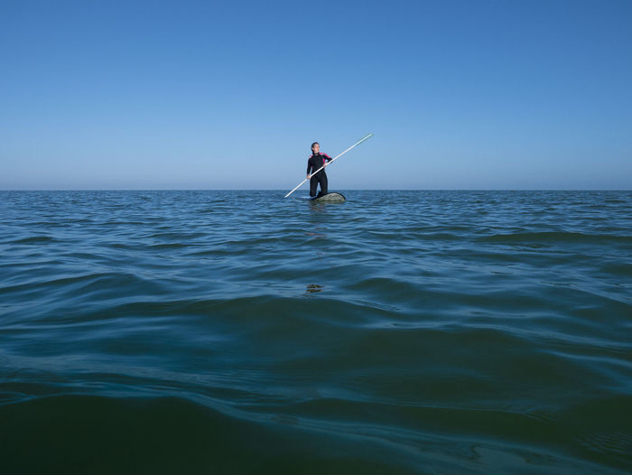 Woman paddleboarding on sea against clear sky