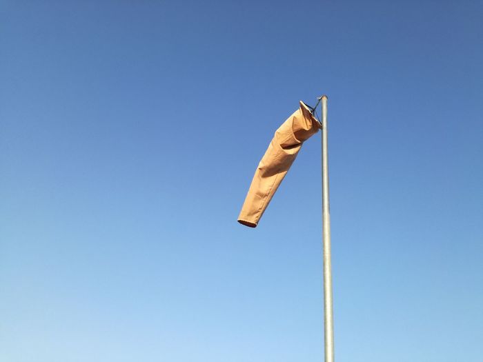 Low angle view of windsock on pole against clear blue sky