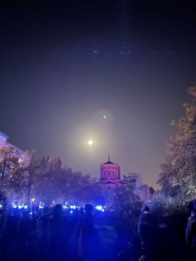 People on illuminated building against sky at night