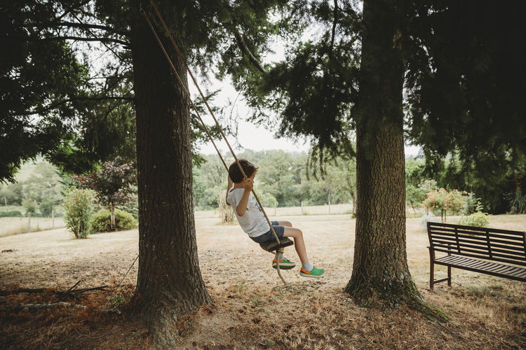 Side view of boy on swing under trees