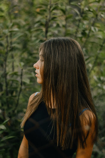 Woman looking away while standing against trees