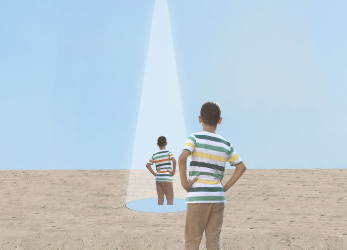 Rear view of men standing on beach against clear sky
