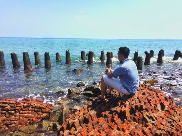 Man sitting on rock by sea