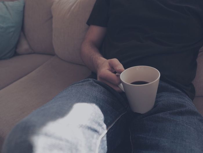 Midsection of man having coffee while sitting on sofa at home
