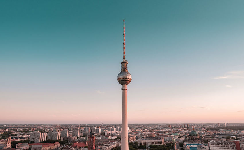 Communications tower in city against sky during sunset