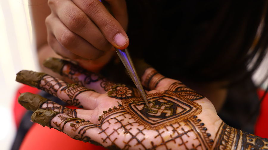 Midsection of woman drawing henna tattoo on hand