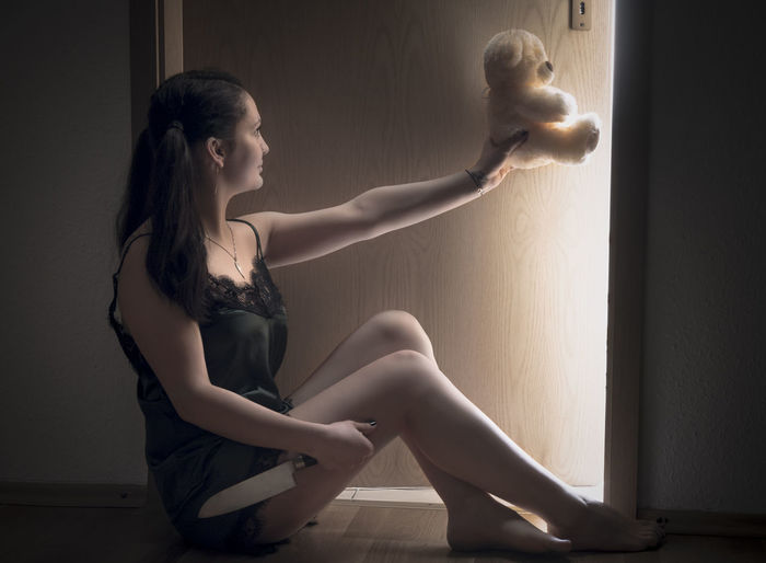 Young woman with teddy bear sitting at home