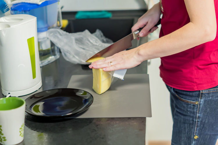 Woman cooking breakfast. cutting of cheese on plastic booard on modern black and white kitchen.