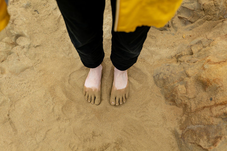 Looking down on young persons feet covered in sand on beach  barefoot