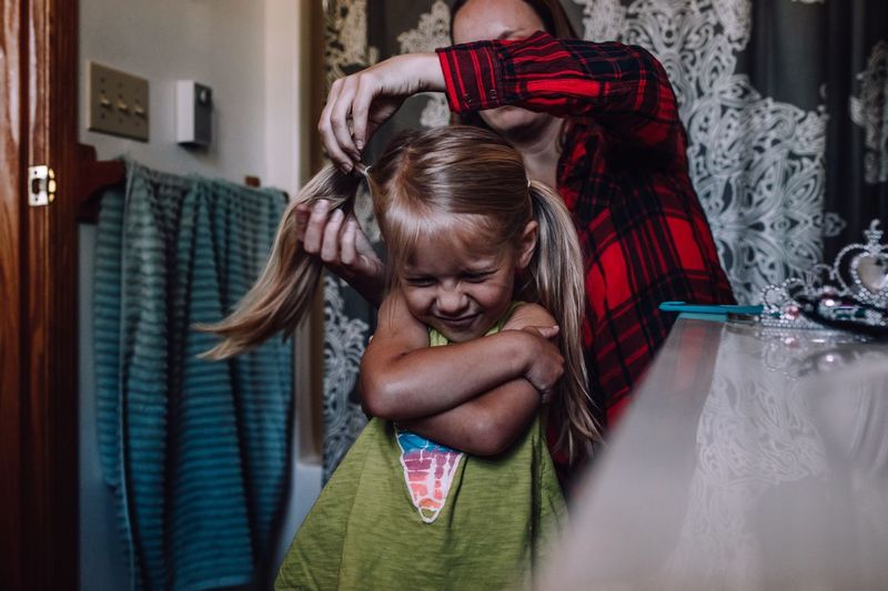 Mother combing hair of daughter at home