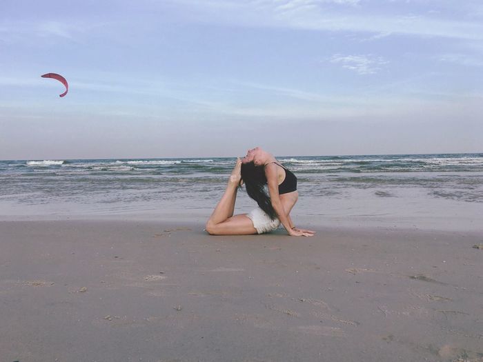 Woman exercising on beach against sky