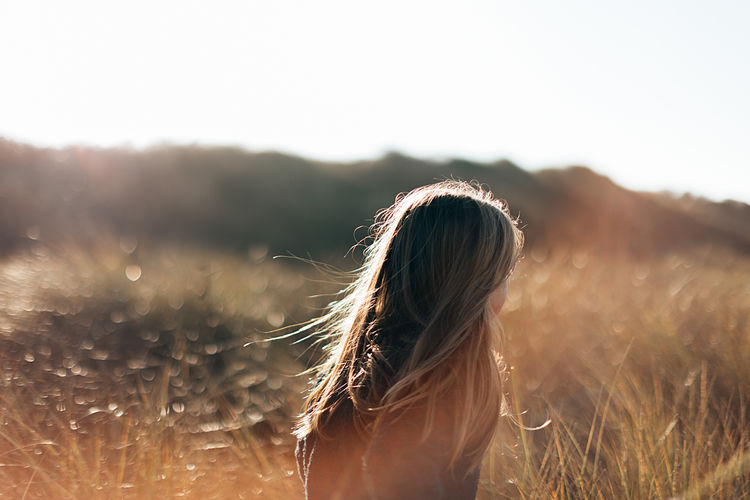 Back view of a young girl with long hair running in a meadow at sunset