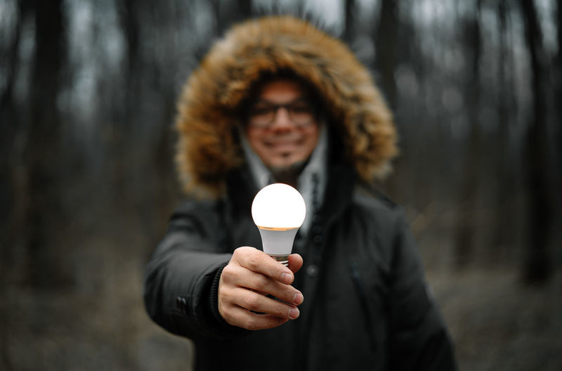 Smiling man holding illuminated light bulb in the forest
