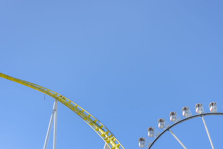 Low angle view of rollercoaster against clear blue sky