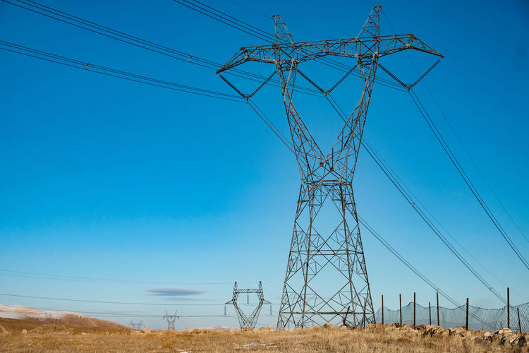 Low angle view of electricity pylon on field against clear sky