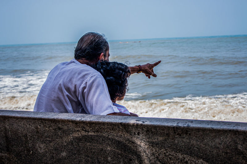 Grandfather with granddaughter looking at sea while sitting on bench