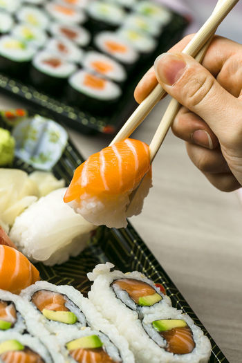 Cropped hand having sushi and sashimi in box on table
