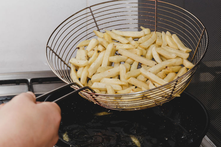 French chips being cooked on a black pan with boiling oil.