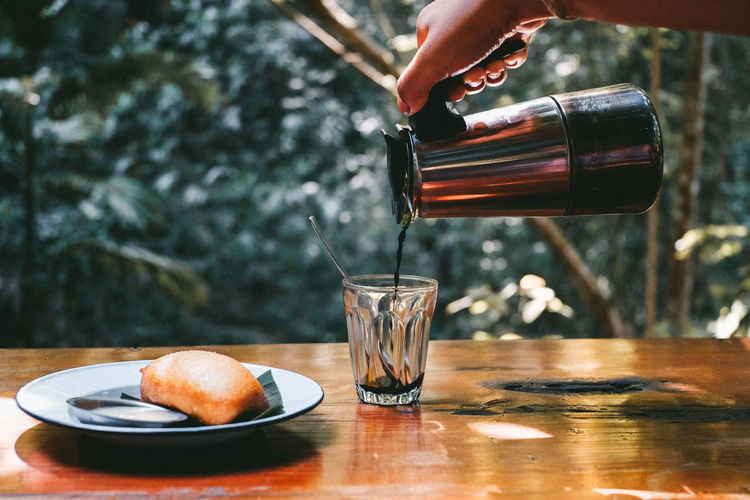 Close-up of hand pouring drink in glass on table
