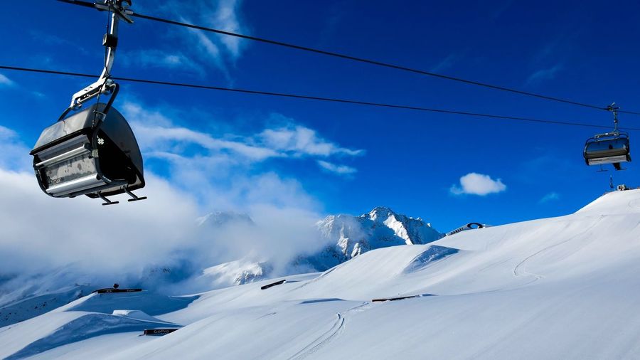 Low angle view of ski lifts over snow covered mountain against sky
