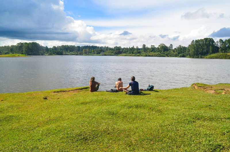 People sitting by lake against sky