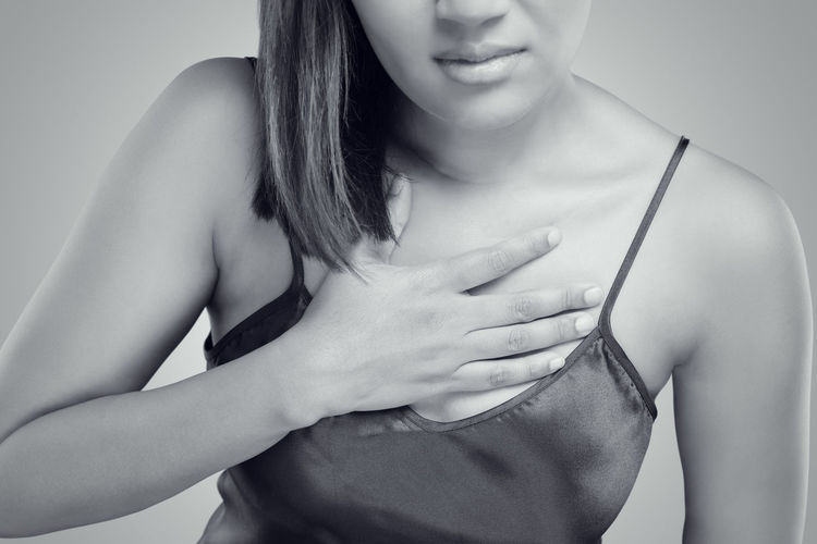 Midsection of woman with hand on chest against gray background
