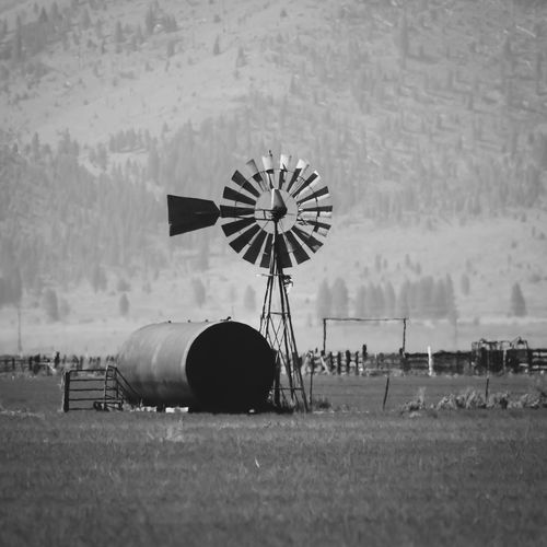Vintage windmill and large water tank on some farmland in monochrome.