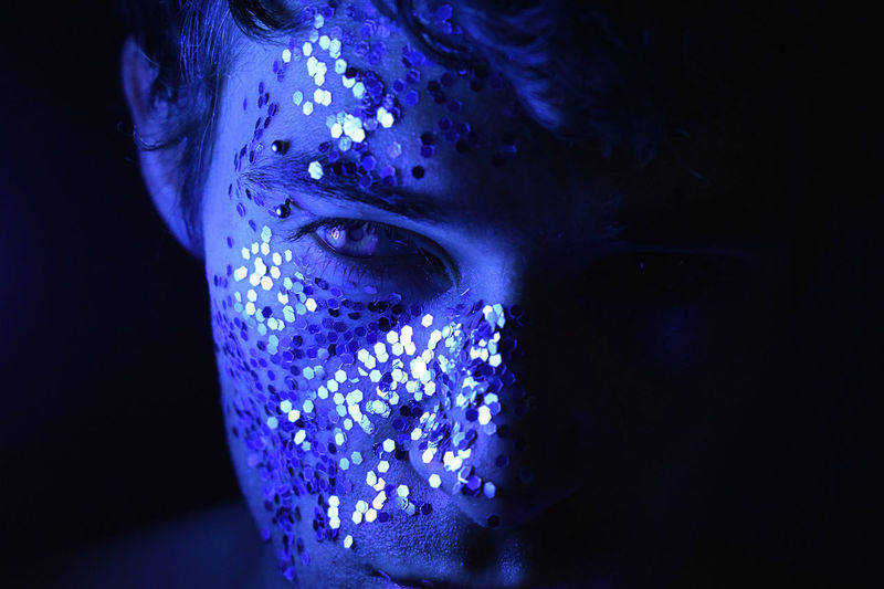 Close-up portrait of man with sequins on face against black background