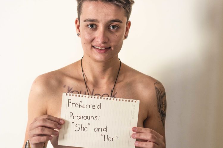 Portrait of shirtless young woman showing paper with text against wall