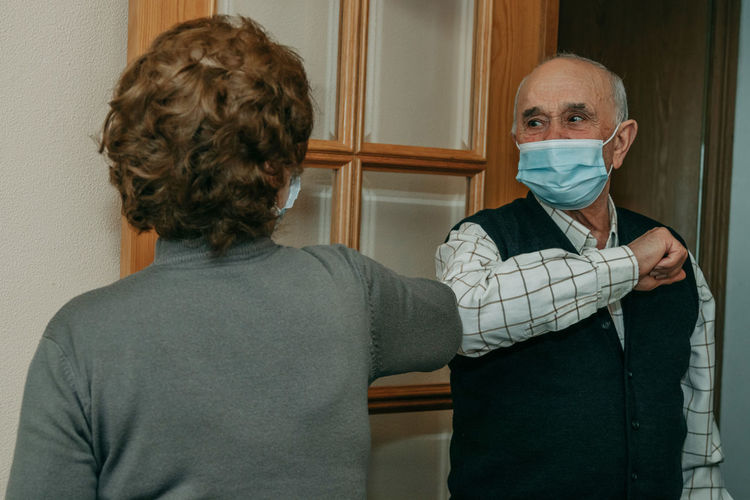 Senior couple wearing mask doing elbow bump at home