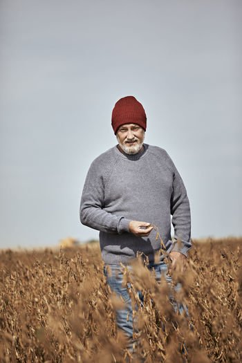 Farmer examining crop while walking in farm against clear sky