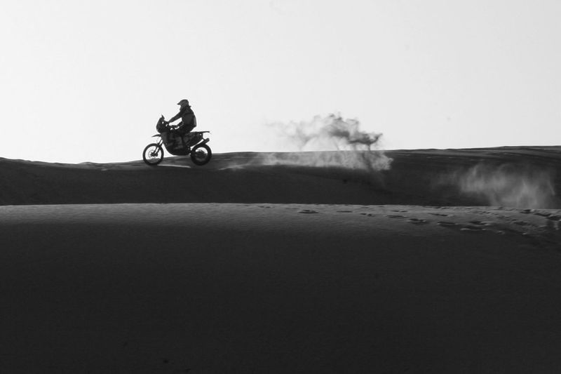 Man riding motorcycle on desert against clear sky