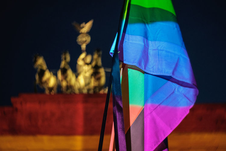 Rainbow flag against brandenburg gate in city at night