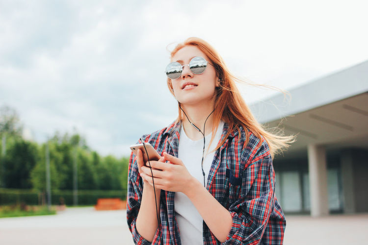 Young woman wearing sunglasses while listening to music in city